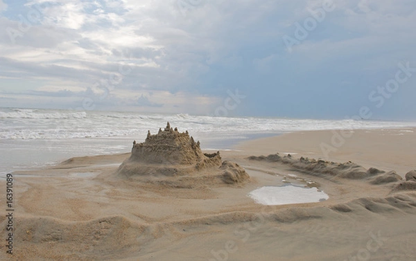 Fototapeta Sand castle built on the beach with moat surrounding it.