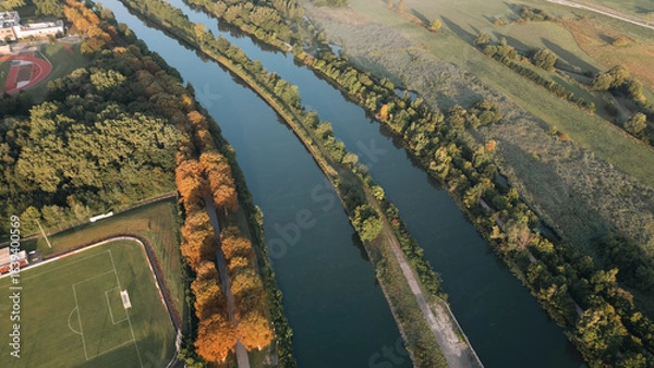 Fototapeta Aerial panoramic view of a river meandering through green fields and rural landscapes in Germany during sunrise, captured by drone.