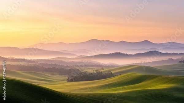 Fototapeta Serene Rolling Hills Under Colorful Sunset Sky with Misty Mountains