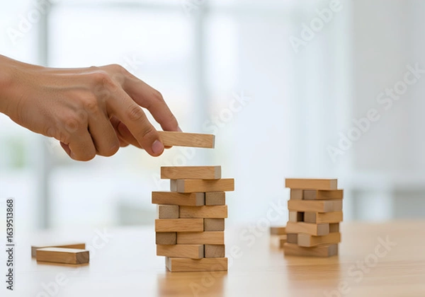 Fototapeta Hand placing a wooden block on a tower. A person carefully builds a tower, representing business strategy, risk management, and planning. The concept illustrates growth, fragile foundations, and skill