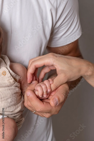 Fototapeta A newborn's hand is attached to the thumb of the mother's hand and supported by the father's hand