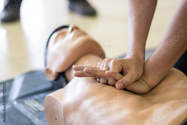Obraz CPR training medical procedure - Demonstrating chest compressions on CPR doll in the class