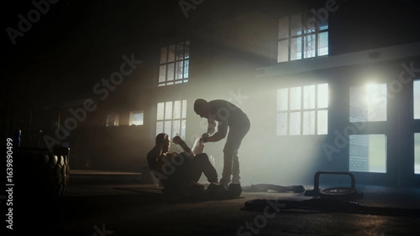 Fototapeta Determined male athletes training together doing sit-ups in dramatic gym