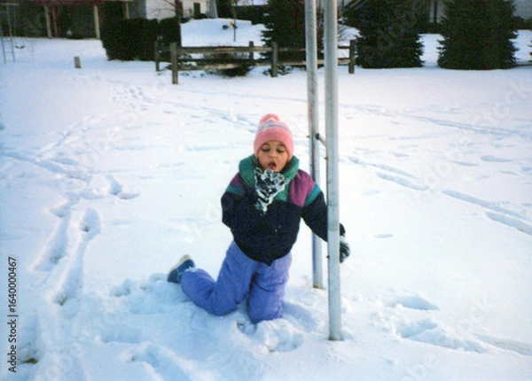 Fototapeta Child in the 80s, playing in the snow, eating snow, wearing a snowsuit. Vintage scan, may have imperfections