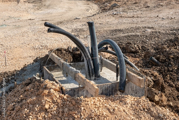 Fototapeta Large black corrugated pipes emerge from a new concrete foundation on a dusty construction site. The unfinished trench indicates the installation of underground infrastructure