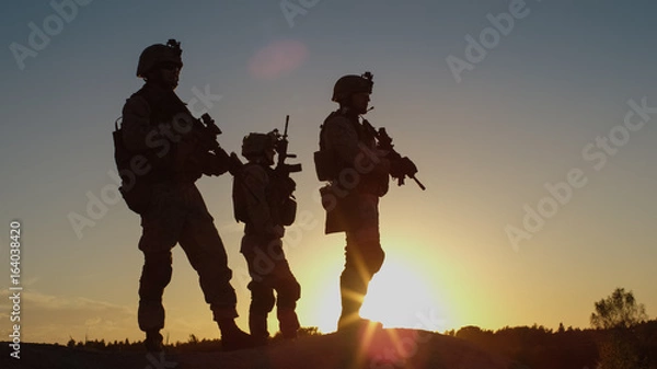 Fototapeta Squad of Three Fully Equipped and Armed Soldiers Standing on Hill in Desert Environment in Sunset Light.