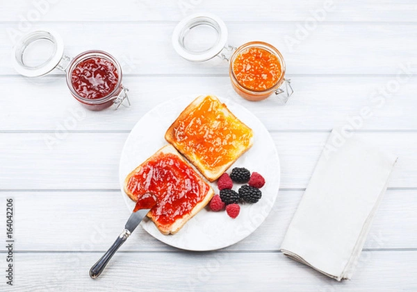 Fototapeta Top view of tasty toast breakfast with strawberry and peach jam along with blackberries and raspberries on wooden table.