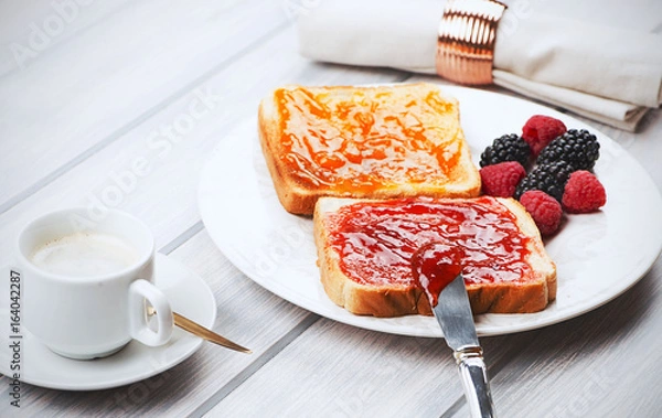 Fototapeta Tasty breakfast of toast with strawberry and peach jam along with blackberries and raspberries, and a cup of coffee.