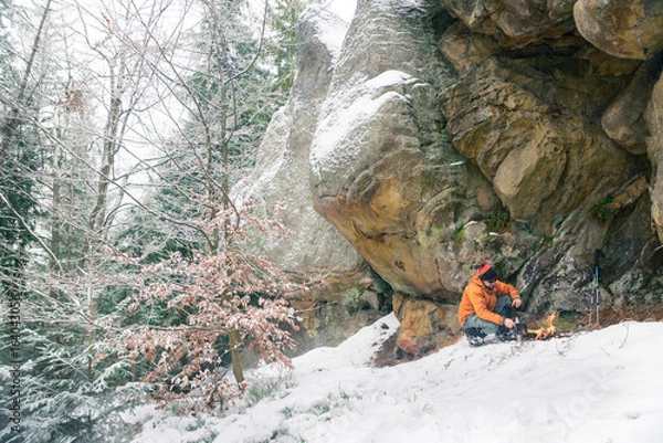 Obraz man preparing food under rock where hiding from snowstorm, survival