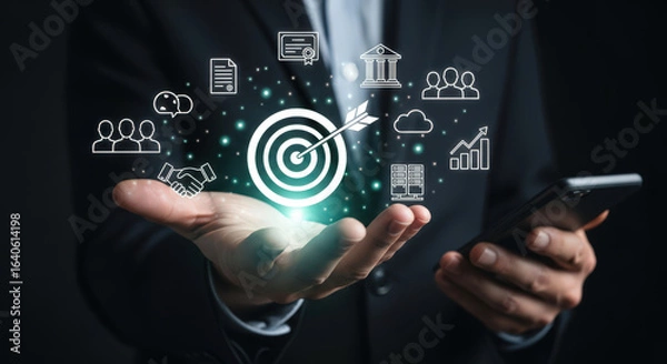 Fototapeta Strategic Business Goals and Objectives Concept with Hand Holding Smartphone Displaying Target Icon and Related Symbols Representing Achievement and Success in Digital Era