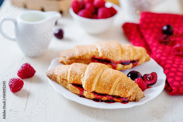 Fototapeta Light and tasty breakfast or lunch, croissants with berry jam, fresh raspberries, cherries, strawberries, black coffee and milk on a light background