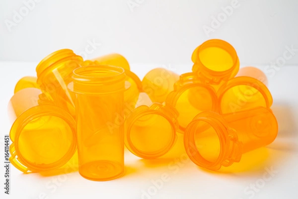 Obraz A dozen Prescription (Rx) vials piled on a white counter, conceptualizing either healthcare or addiction/substance abuse