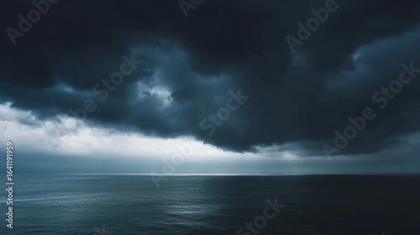Fototapeta A dramatic seascape under dark, moody clouds, with a hint of light reflecting off the calm water, creating a serene yet ominous atmosphere.