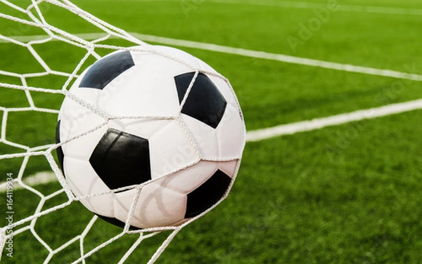 Fototapeta Soccer football in Goal net with green grass field.