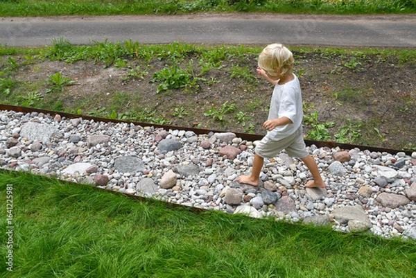 Fototapeta Barefoot boy walking on a sensory trail through a sunny pine forest in summer