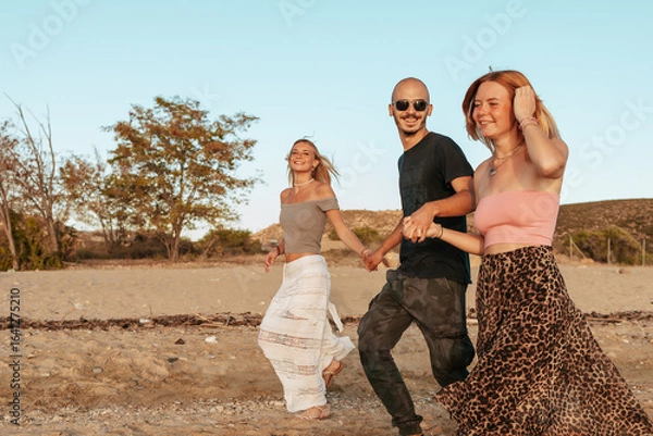 Fototapeta Three happy friends running on the beach at sunset in Potos, Thassos