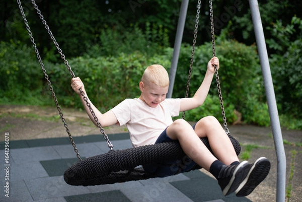 Fototapeta Smiling boy on swing - real-life emotion in the park.
