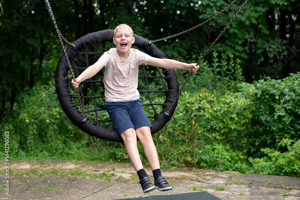 Fototapeta Boy on swing laughing loudly - real-life emotion in the park.