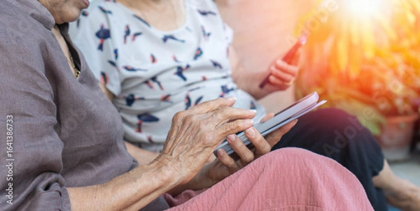 Fototapeta Asian elderly woman using a smartphone interacts with the screen or taking selfie reflecting the growing connection between seniors and digital technology.