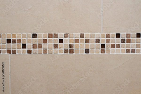 Fototapeta Mosaic tiles in earthy browns and creams create a decorative border on beige tiled wall, adding stylish touch to interior wall designs for bathrooms, kitchens, and other stylish spaces