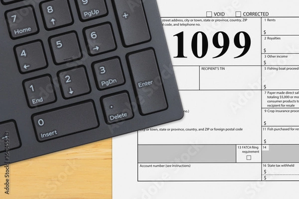 Fototapeta Federal tax 1099 form with a computer keyboard on a wood desk