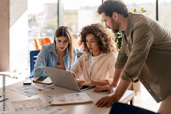 Fototapeta Marketing team analyzing data and collaborating on laptop in office meeting