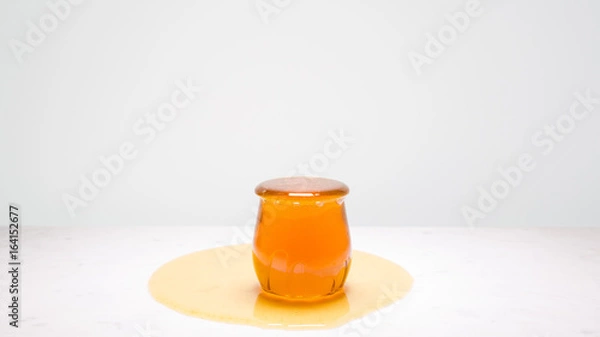 Fototapeta My cup runneth over - a jar overflowing with honey on a white marble countertop and copy space above, to the left and right.