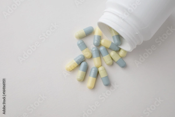 Fototapeta Top view white bottle container with medication capsules on light grey background with copy space.