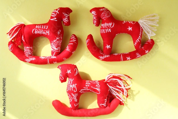 Fototapeta Three red horses sewn from fabric. Concept - New Year's tree toy, handmade in Tilda style. Yellow background, sun glare.