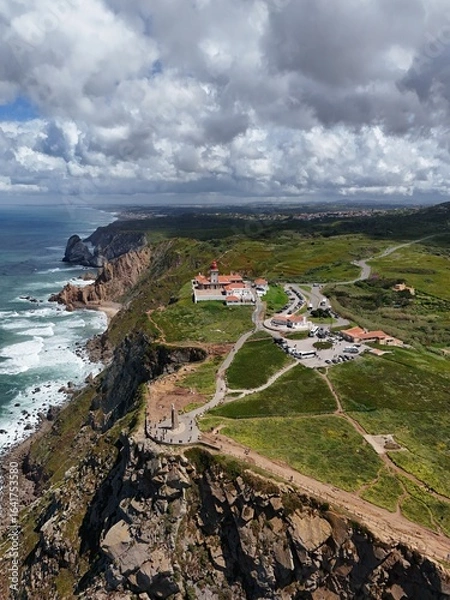 Fototapeta 4K Aerial Drone Footage of a Rugged Coastal Landscape Featuring a Lighthouse, Ocean Waves, Cliffs, and Green Hills Captured in Natural Daylight