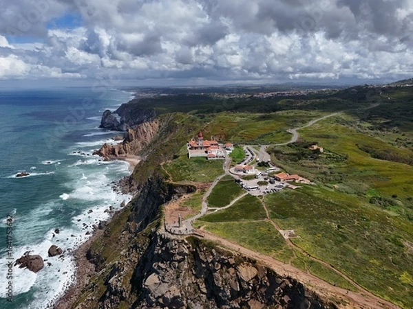 Fototapeta 4K Aerial Drone Footage of a Rugged Coastal Landscape Featuring a Lighthouse, Ocean Waves, Cliffs, and Green Hills Captured in Natural Daylight