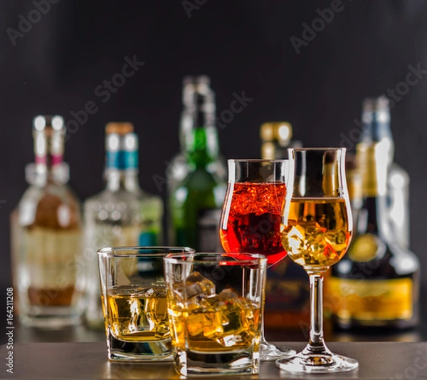 Fototapeta Colorful drink on the background of bottles in original shapes, cocktail drink with ice cubes