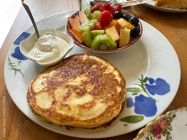 Fototapeta Delicious breakfast plate featuring fluffy pancakes served with fresh fruit salad and creamy yogurt on a rustic wooden table, showcasing a vibrant and inviting morning meal experience