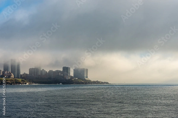 Fototapeta Morning view of Mar del Plata city with buildings partially covered by fog, facing the Atlantic Ocean. Urban and coastal scenery with natural atmosphere.