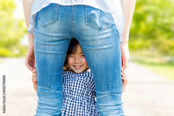 Obraz お母さんの後ろ姿の股から覗く笑顔の幼い女の子