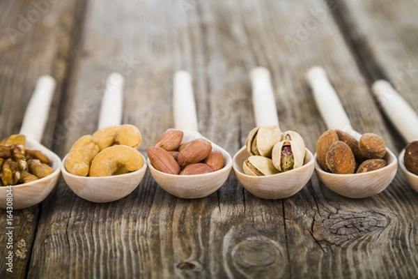 Fototapeta Nuts in a wooden spoons on a  wooden table.