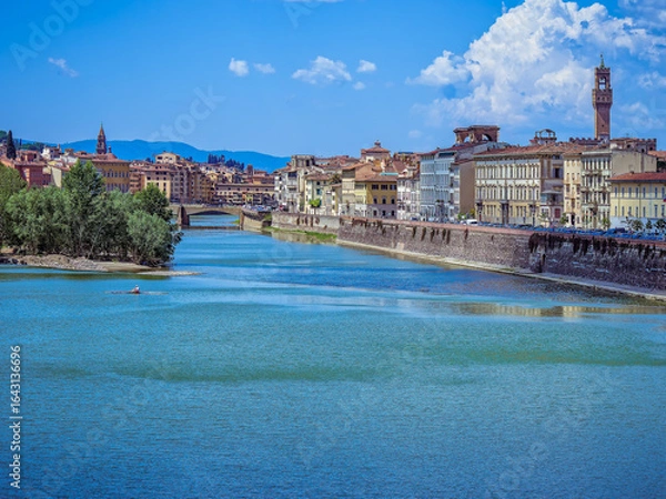 Fototapeta Lungarno della Zecca runs alongside the Arno, with the belfry of Santa Maria della Croce standing gracefully in the background, adding a touch of historic elegance to the Florentine riverside.