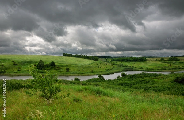 Obraz Cloudy summer scene with small river. Dramatic sky over the fields