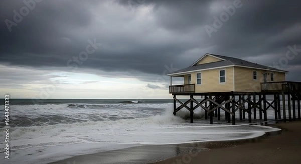 Fototapeta Beach house on stilts facing stormy ocean with dark clouds and crashing waves during a hurricane.