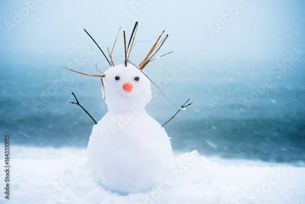 Fototapeta Little cute snowman with carrot nose on blue sea background on snow in winter. Holiday background with cute snowman. Christmas card, copy space.