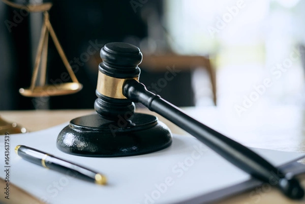 Fototapeta A wooden gavel rests on a stack of documents beside a laptop, symbolizing power and justice.
