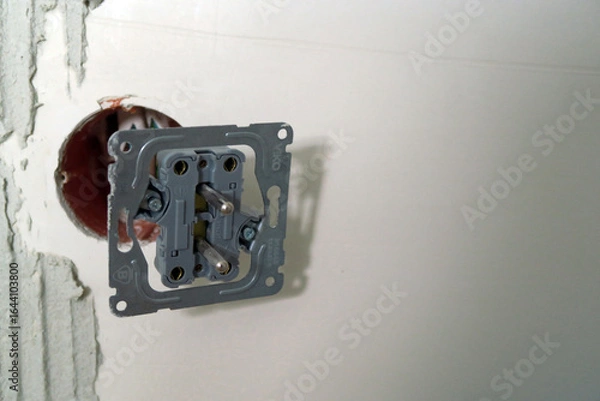 Fototapeta A partially installed electrical outlet is mounted on a white wall, with exposed wiring and an unfinished hole, indicating ongoing electrical work.