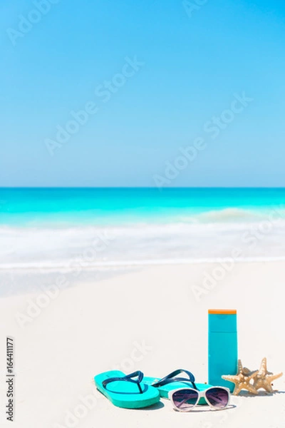 Fototapeta Beach accessories needed for sun protection. Suncream bottles, goggles, flip flops, starfish on white sand beach background ocean
