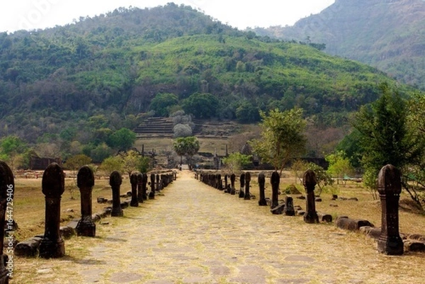 Obraz Ancient stone pathway leading to Wat Phou temple with lush green hills in the background