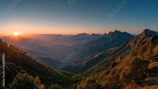 Fototapeta Panoramic sunset view over a vast mountain range, layers of hazy hills fading into a clear sky, sun's rays casting a golden glow on the landscape