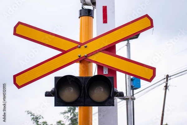 Fototapeta Close up view of a railway level crossing, marked by a prominent yellow and red X sign and a traffic light system.