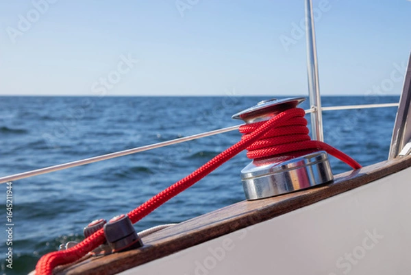 Fototapeta Sailboat winch with red rope of genoa headsail sheet in jammer on yacht deck. Detailed close-up with shallow depth of field, highlighting sailing equipment, marine life, and nautical craftsmanship