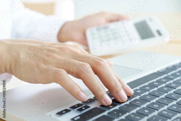 Fototapeta Businessman working at a computer and finds the calculator n the office workplace