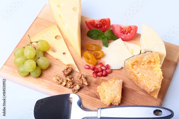 Fototapeta Assortment of cheese with fruits, grapes, nuts and cheese knife on a wooden serving tray.