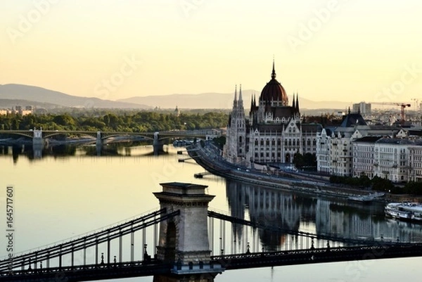 Fototapeta the Hungarian Parliament in Neo-Gothic style across the Danube in panoramic view. Famous and popular Budapest landmark and tourist attraction. the Chain bridge in the foreground City skyline. blue sky